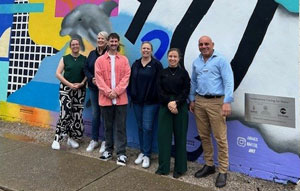 Four people dressed casually standing against a graffiti type mural 