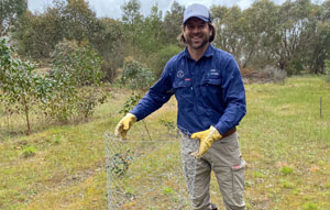 A man in outdoor clothing holding a roll of steel mesh fencing in a field