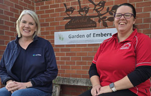 Two females sitting on a bench looking t the camera, smuling